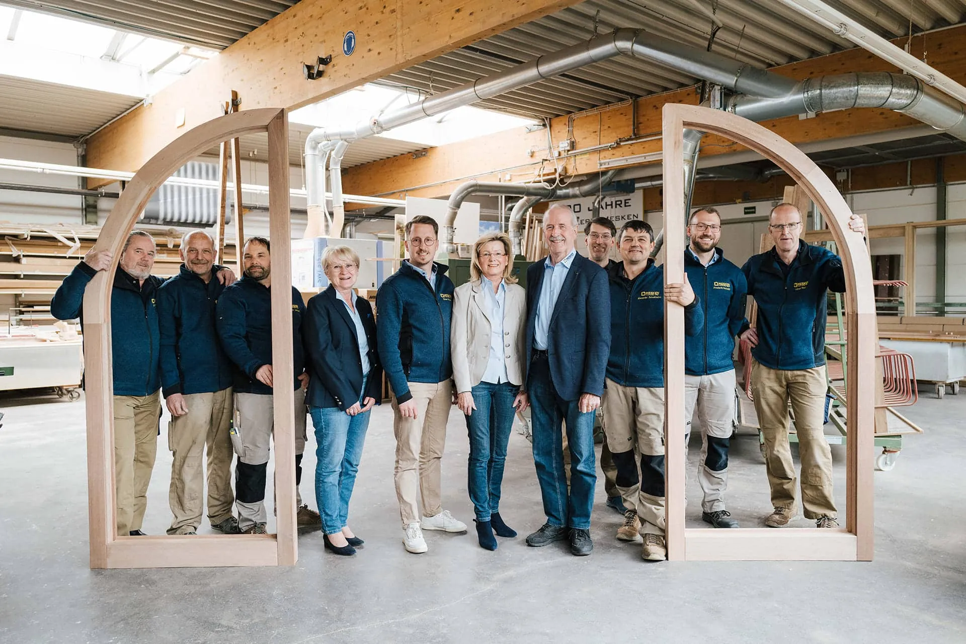 Team einer Schreinerei in Werkstatt mit großem Holz-Bogenrahmen für Fenster